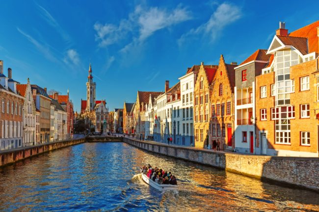 Tourist boat on canal Spiegelrei, Bruges, Belgium Tourist boat on canal Spiegelrei and Jan Van Eyck Square in the morning in Bruges, Belgium