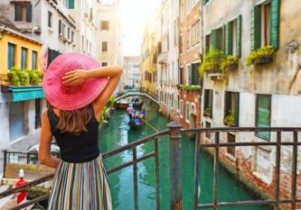 Frau mit rotem Sonnenhut schaut auf einen Kanal mit Gondel in Venedig, Italien Frau mit rotem Sonnenhut schaut auf einen Kanal mit Gondel in Venedig, Italien